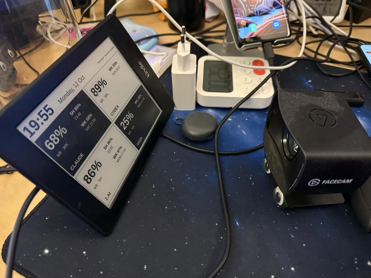 A Kindle on a desk shows the first landscape dashboard, with a large clock and black tiles, next to a webcam.